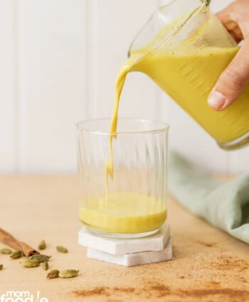 Pouring brewed golden milk into serving glass.