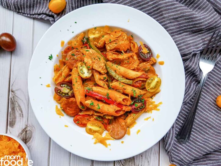 Serving Cajun Chicken Pasta with Peppers and Sausage on white plate with tomatoes and cheese on top