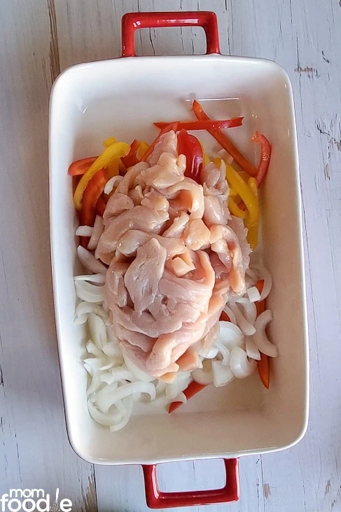 sliced peppers,  onions , pieces of chicken  breasts in casserole dish