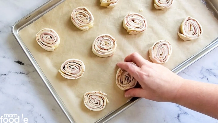 Placing cold pinwheels on lined baking sheet.