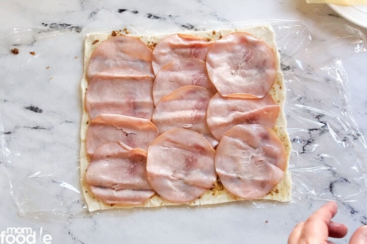 Arranging sliced ham over the dressing. Layer the meat evenly.