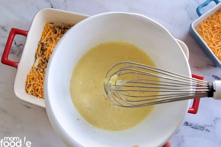 beat eggs, milk and seasonings together with a whisk, shown in white deep bowl.