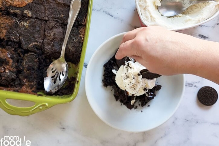 putting whipped cream and more oreos on top of the dump cake