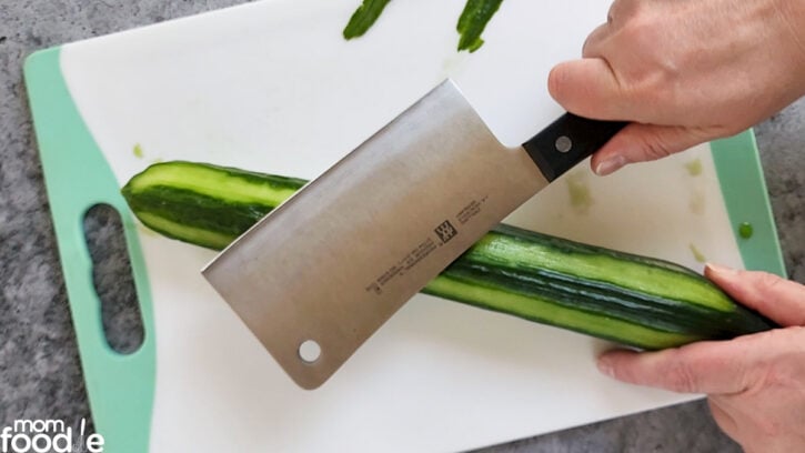Smashing cucumber with the flat side of a heavy cleaver, while holding end for stability.
