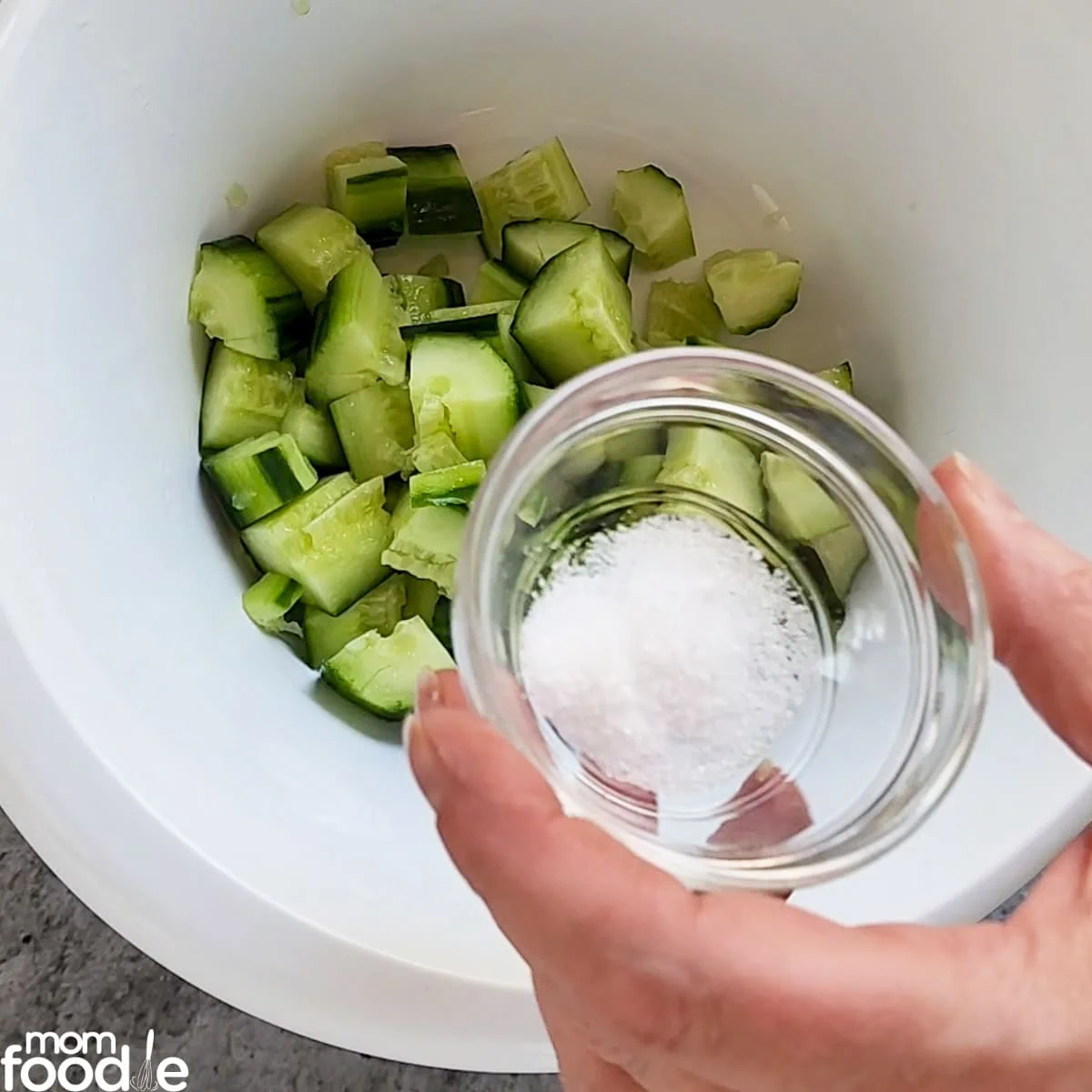 pouring salt on the chopped cucumbers in bowl