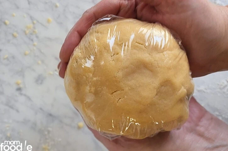 Wrapping pie dough ball in plastic wrap.