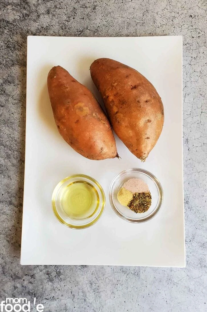 Ingredients to make the air fryer sweet potato fries laid out on a platter; sweet potatoes. oil and seasoning.