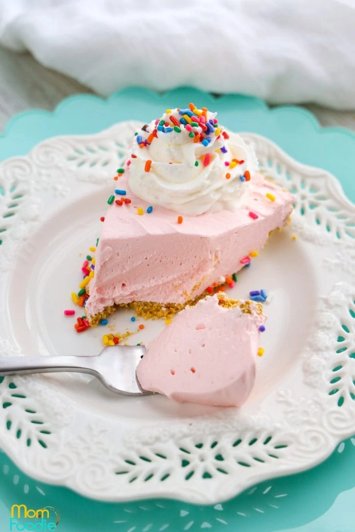 pink Kool Aid Pie on plate with candy sprinkles and whipped cream.