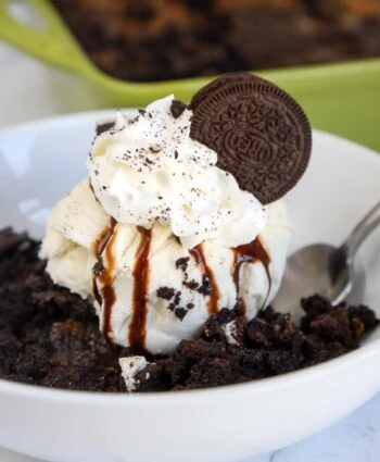 Oreo Dump cake with ice cream, chocolate syrup, whipped cream, crushed Oreo cookies and a whole cookie on top.