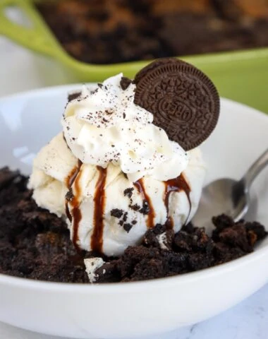 Oreo Dump cake with ice cream, chocolate syrup, whipped cream, crushed Oreo cookies and a whole cookie on top.