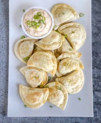 Air Fryer Pierogies on white platter with sour cream sauce and sliced green onions