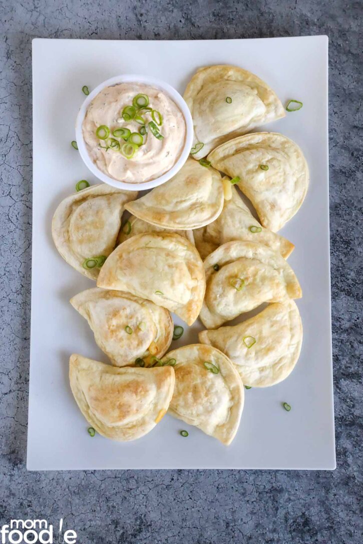 Air Fryer Pierogies on white platter with sour cream sauce and sliced green onions