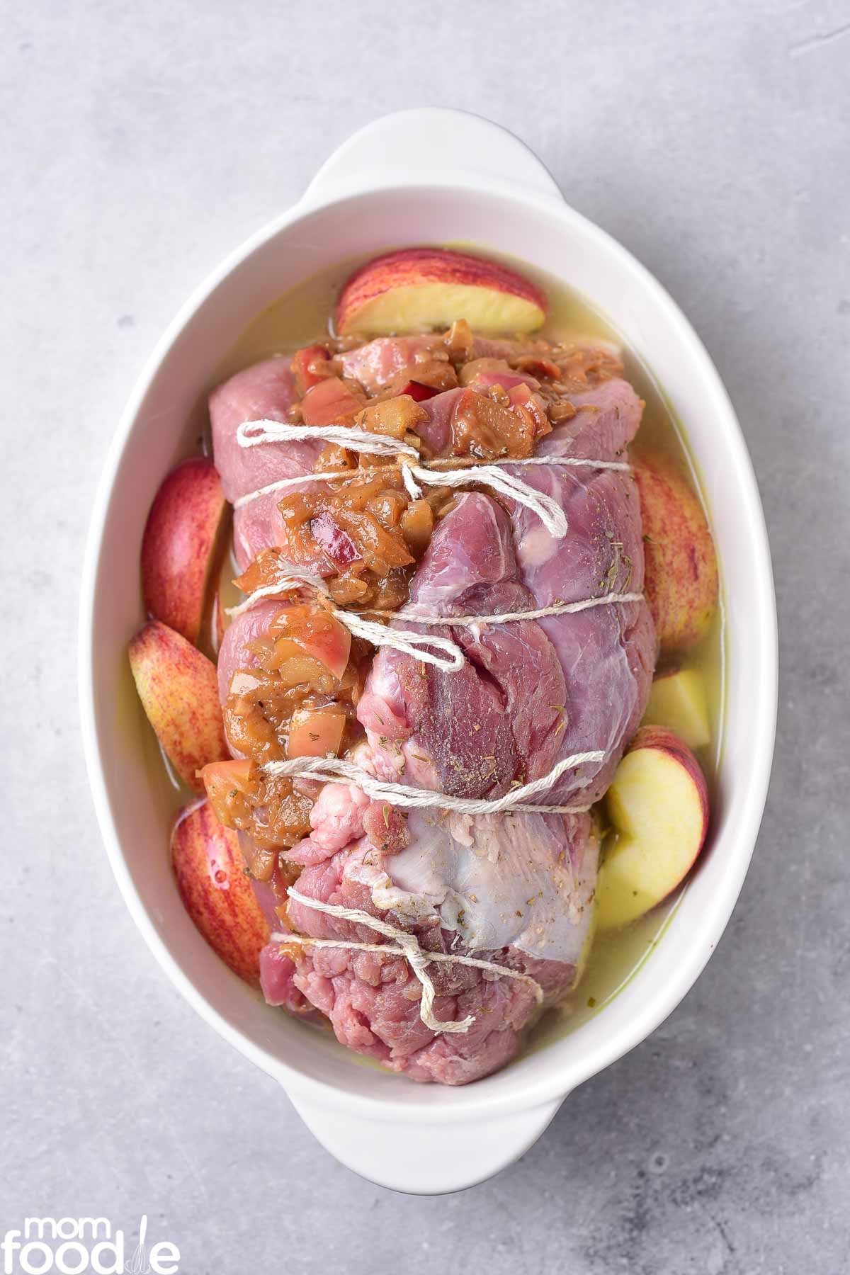 roast tied with kitchen string in casserole dish with broth and extra apples