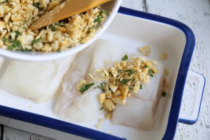adding cracker topping to baked cod filets.