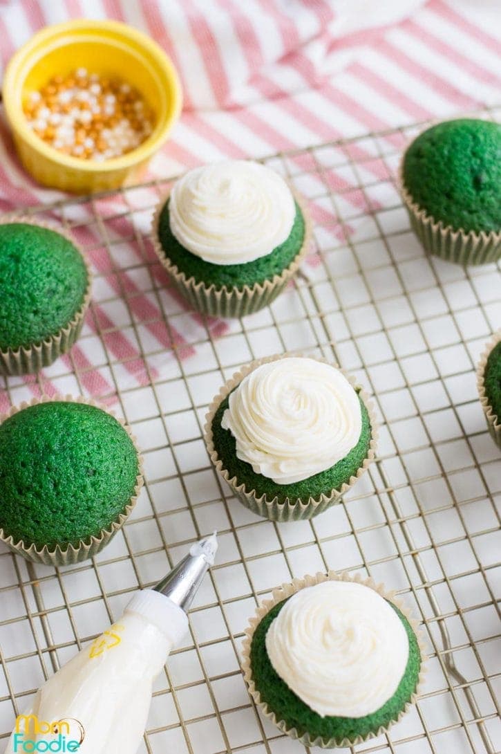 piping cream cheese frosting onto the green cupcakes