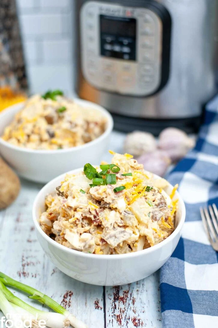 Instant Pot Potato salad loaded with bacon and cheese in bowls in front of Instant Pot.