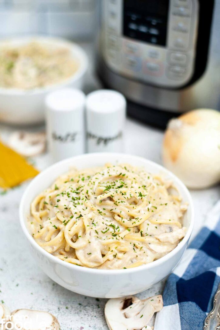 Instant Pot Chicken Tetrazzini shown in bowl in front of pressure cooker.