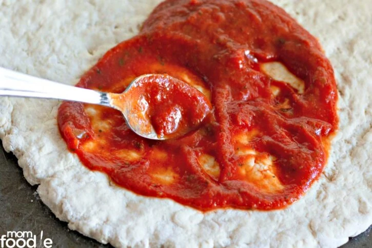 Topping two ingredient pizza dough with sauce, spread evenly.