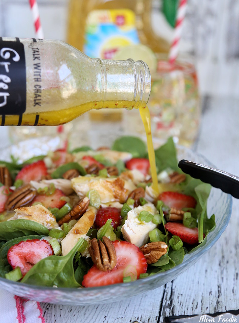 Green Tea Honey Vinaigrette pouring over the bowl of strawberry chicken spinach salad with pecans