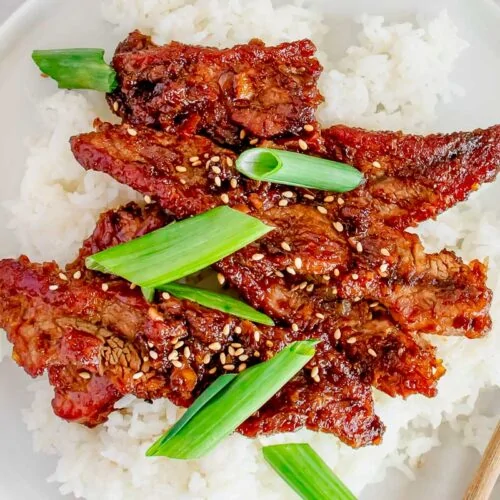 Mongolian Beef Recipe shown plated over steamed rice with chopsticks.