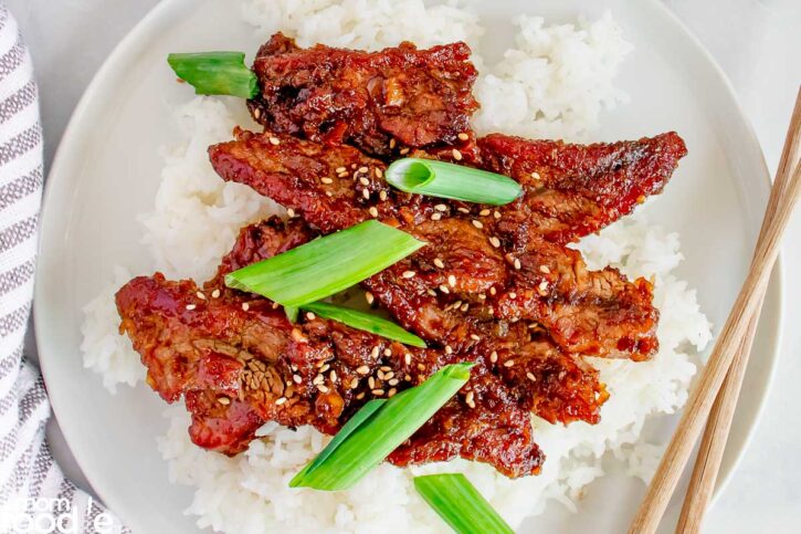 Mongolian Beef Recipe shown plated over steamed rice with chopsticks.