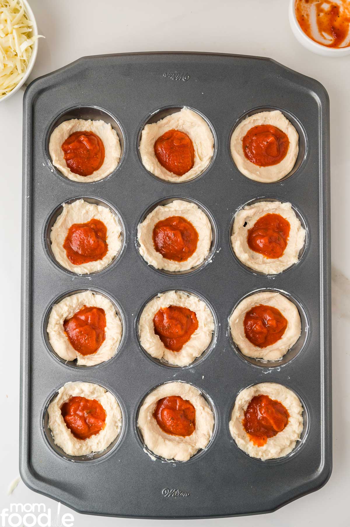 tomato sauce spread over center of the dough in muffin cups