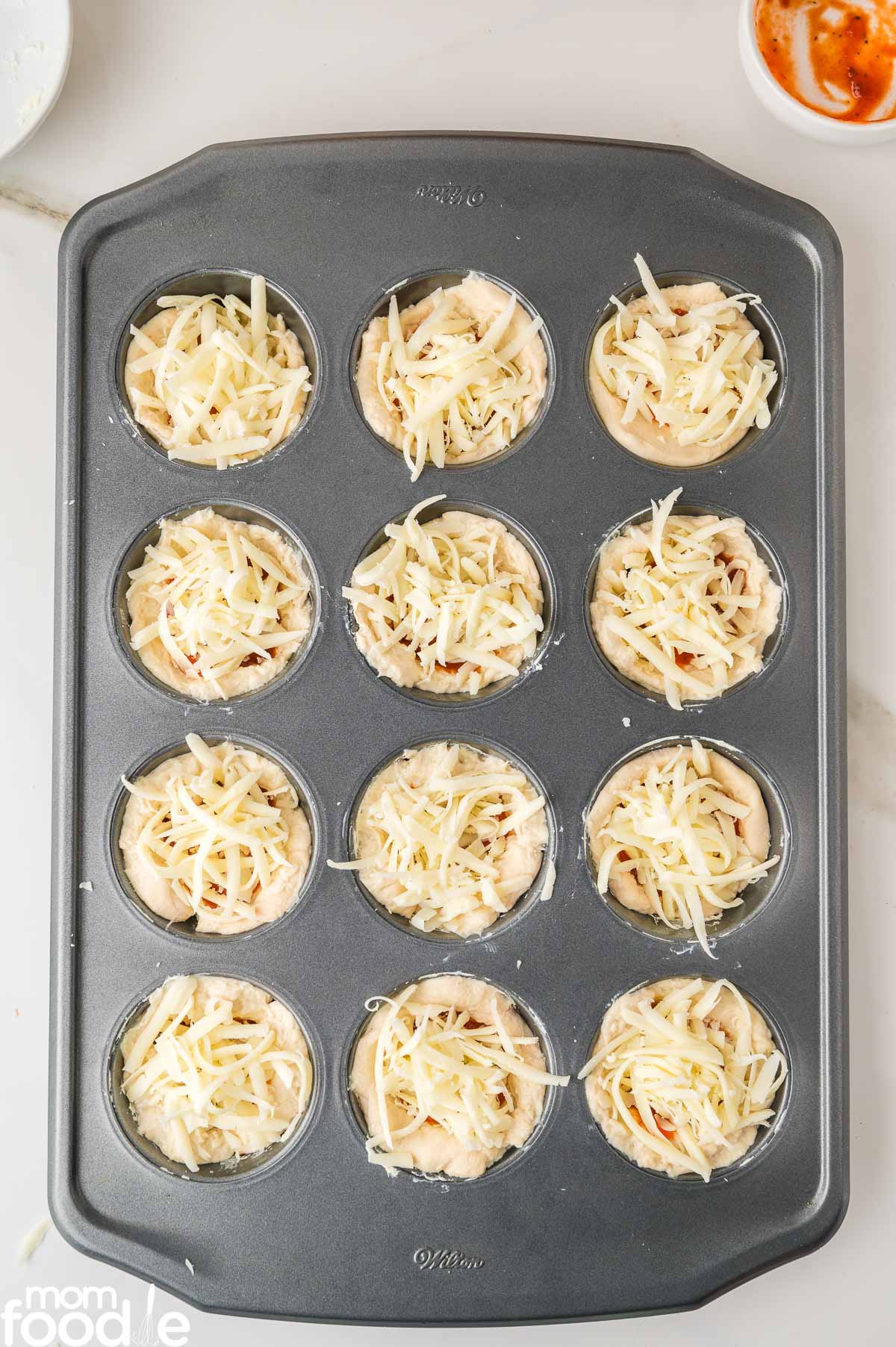 topping the mini pizzas with shredded cheese