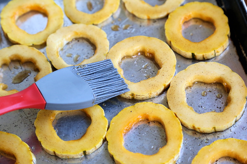 using a basting brush to coat  squash with oil and salt plus seasonings to prepare for roasting.