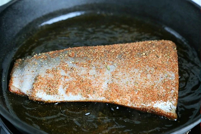 blackened salmon filets cooking skin side up in hot skillet