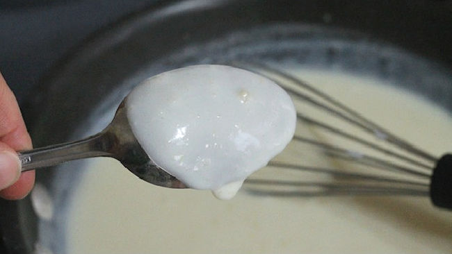 testing thickness of sauce for broccoli cheese casserole using the back of a spoon.