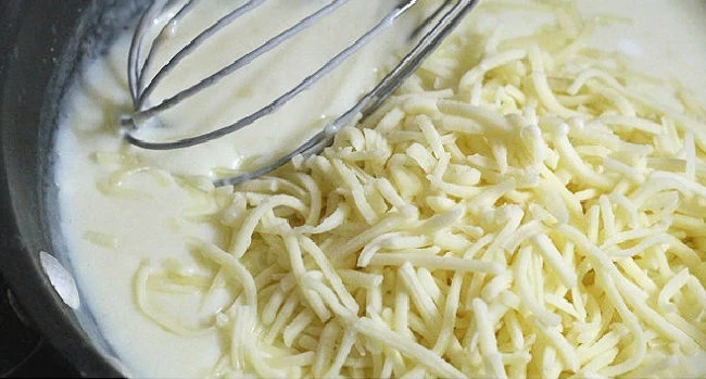 Shredded cheese added to white sauce about to be gently whisked in to melt.