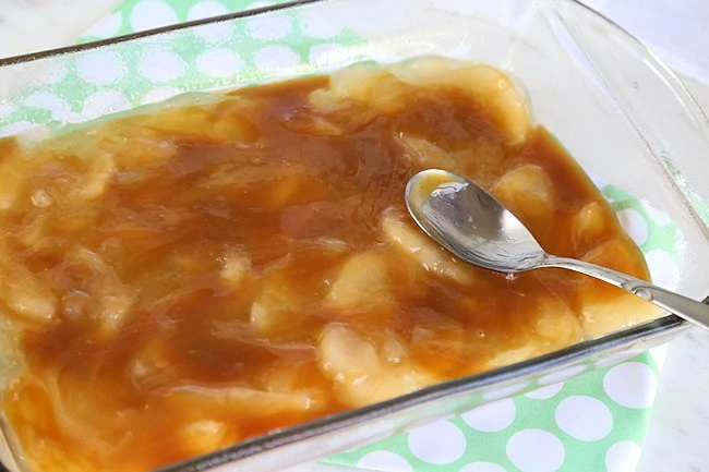 Caramel sauce layer being spread out on top of apples with the back of a sppn.