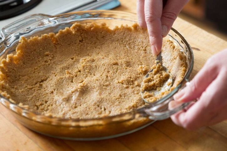 making graham cracker crusts, shows step of the graham crackers mixture being spread out with spoon in glass pie dish