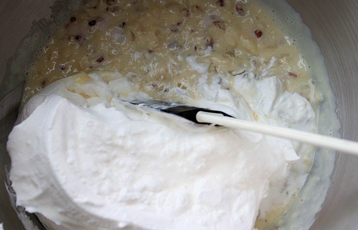 filling ingredients being mixed in large bowl with spatula, sweetened condensed milk, pineapple, lemon juice, toasted coconut, pecans and whipped topping