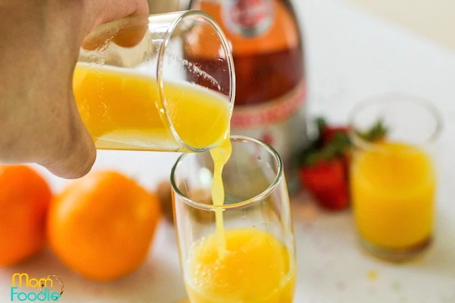 pouring orange juice in glass for mimosa