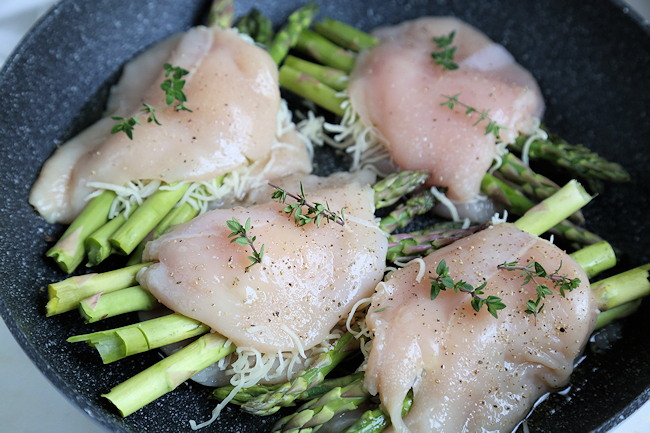 four raw stuffed chicken breasts with asparagus and cheese in skillet ready to cook.