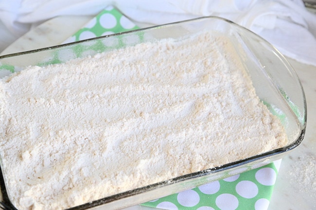 Yellow cake mix spread out on top of apples and caramel to edges of pan for dump cake.